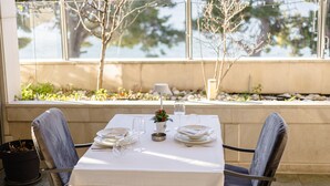 A table set for dining with chairs, a small potted plant, and a glass of water. - Rogač Rooms & Restaurant (Dugi Rat)