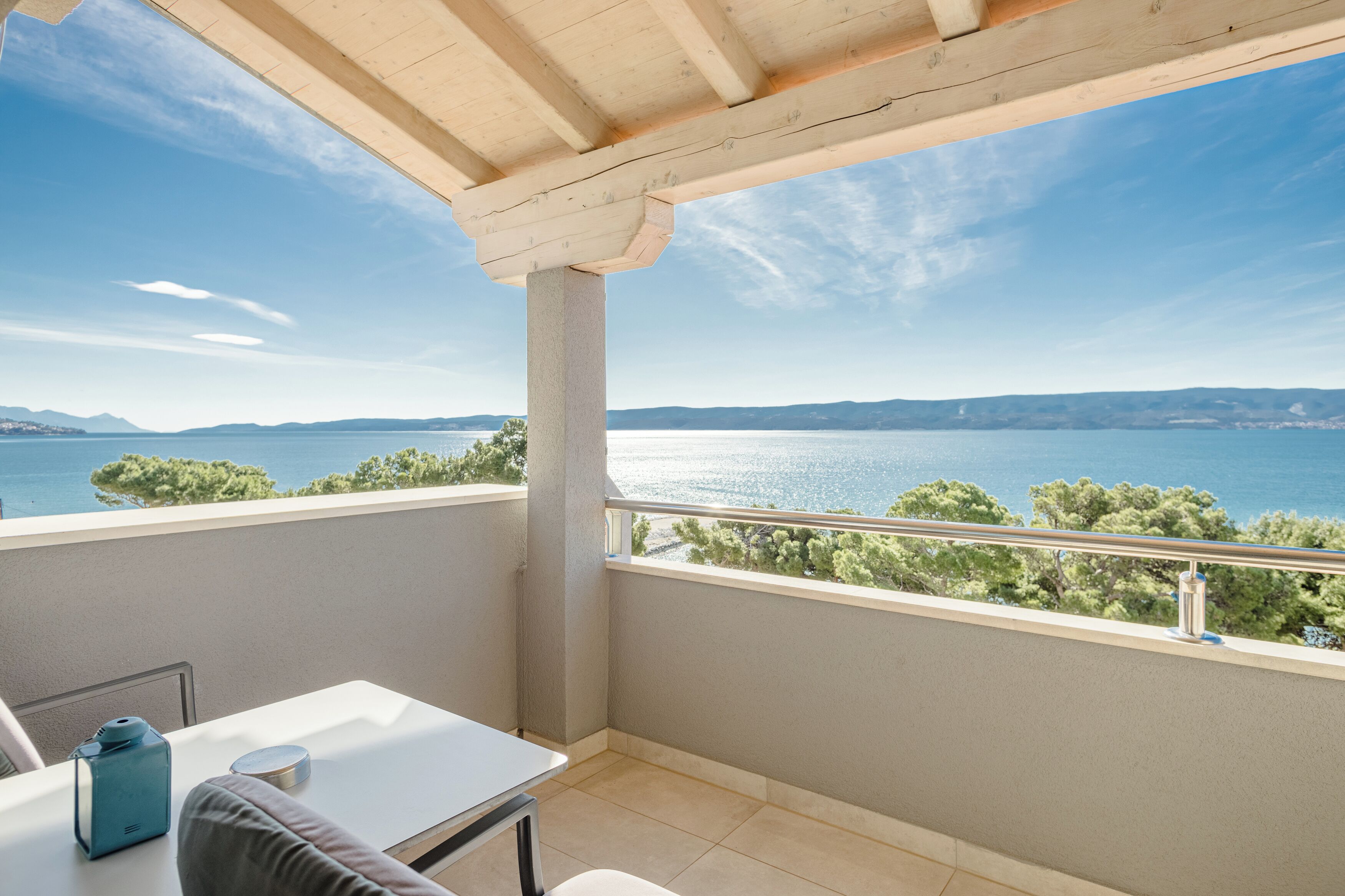 A balcony with a view of a lake and mountains, a table, and a chair.