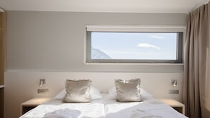 A double bed with two pillows, a window with a mountain view, and a bedside table with a lamp. - Rogač Rooms & Restaurant (Dugi Rat)