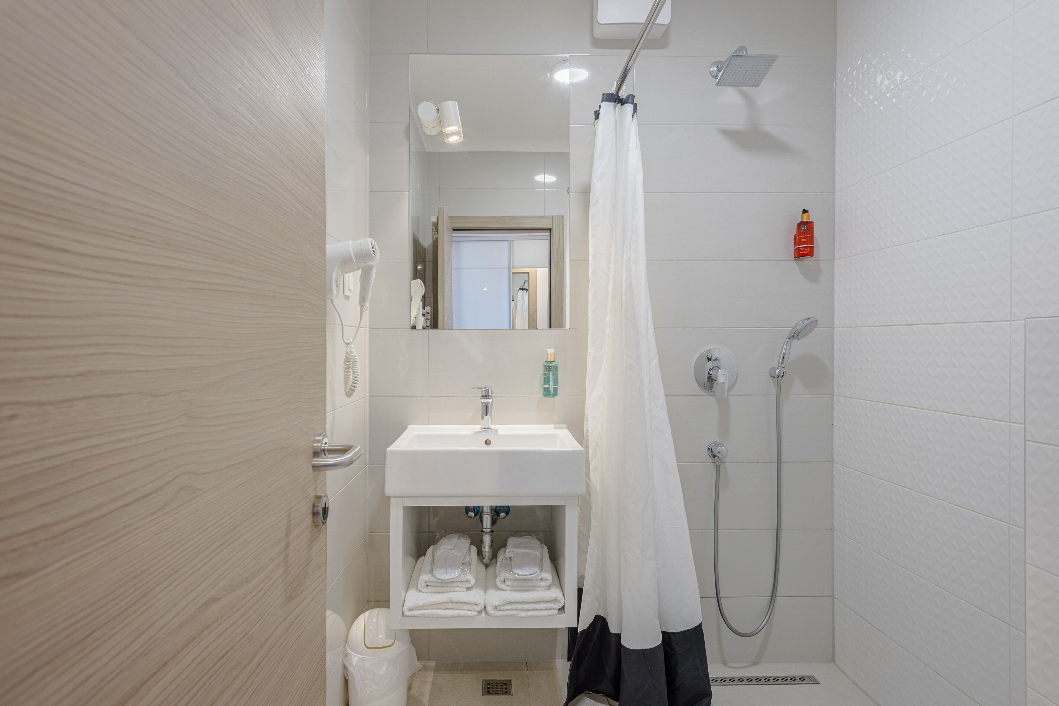 A modern bathroom with a shower, sink, and mirror. There are towels and toiletries visible.