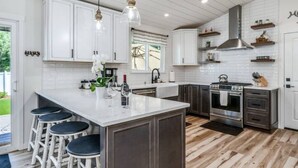 A modern kitchen with white cabinets, a central island with bar stools, stainless steel appliances, and pendant lighting. - Stunning New Horse and Hare Inn (Murphys)