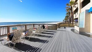 Eine Terrasse mit Liegestühlen mit Blick auf einen Strand, ein Pool und ein Gebäude mit blauen Akzenten.
