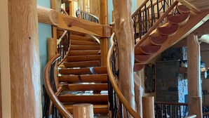 A spiral wooden staircase with a rustic design, surrounded by wooden beams and railings. - Cayuga Lodge  (Cooperstown)