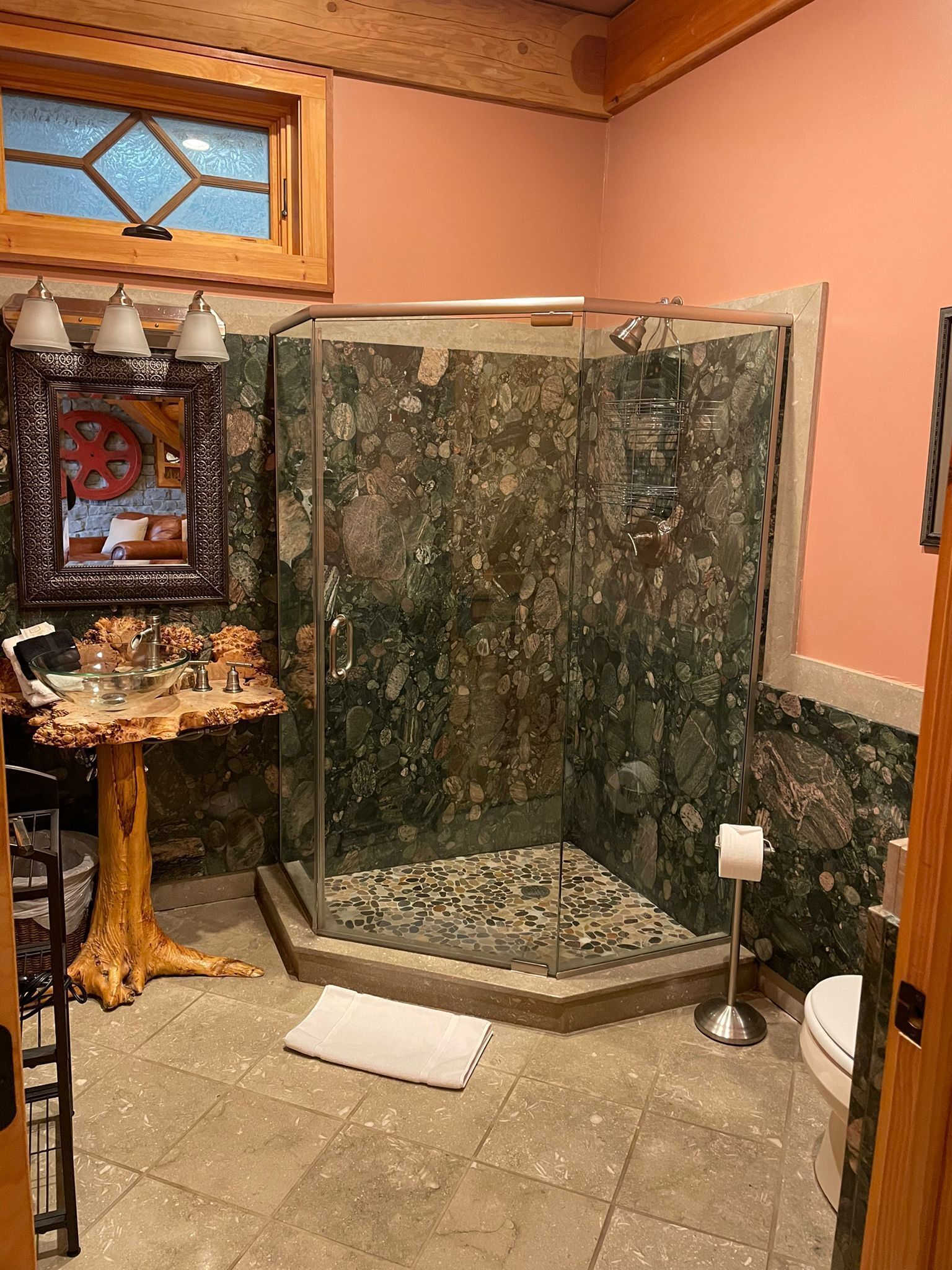 A bathroom with a glass-enclosed shower, a wooden vanity with a bowl sink, and a mirror with a decorative frame.