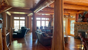 A spacious log cabin interior with a fireplace, leather seating, and large windows. - Cayuga Lodge  (Cooperstown)