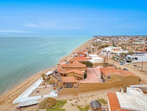 Uma área residencial costeira com casas de telhado vermelho, uma praia e vista clara do mar.