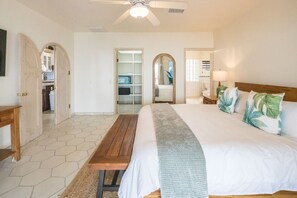 Quarto com cama grande, banco de madeira e ventoinha no teto. Há portas em arco que dão acesso a outros cômodos.