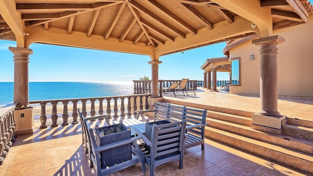 Ein überdachter Außenbereich mit Meerblick, ausgestattet mit einem Tisch und Stühlen, sowie ein Balkon mit Geländer.