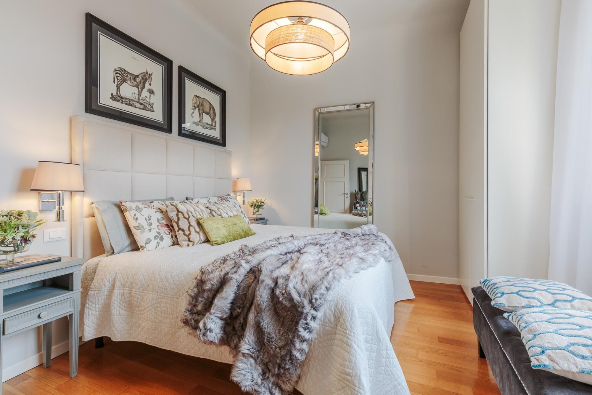 A bedroom with a large bed, a nightstand, a mirror, and framed animal prints on the wall.