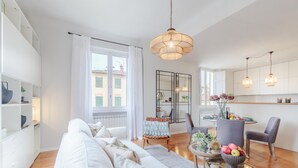 A modern living room with a sofa, a dining table with chairs, and a kitchen area with cabinets and a hanging light fixture. - Casa Buccellato in Lucca (Lucca)