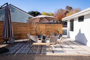 Un patio con una mesa y sillas, una cerca de madera y una casa al fondo.