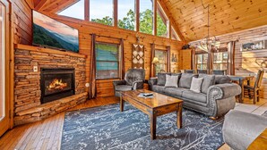 L’intérieur chaleureux d’un chalet avec une cheminée en pierre, des murs en bois, une grande fenêtre et un coin salon confortable.