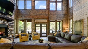 Un salón amplio con chimenea, sofás de cuero y ventanas grandes que ofrecen vistas al exterior.