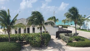 A beachfront property with a modern building, palm trees, and a clear view of the ocean. - Infinity Poolside -  Two story Oceanview 3 Bedrooms / 3 Baths (Bimini)