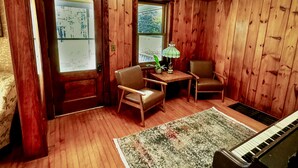 A room with wooden walls and floors, a piano, two chairs, a small table with a lamp, and a rug. - Northstar Lodge - 4000 sq ft + Year-Round Hot Tub (Marquette)