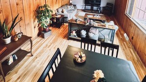 A cozy living room with wooden walls, a sofa, a dining table with chairs, and a television. - Northstar Lodge - 4000 sq ft + Year-Round Hot Tub (Marquette)