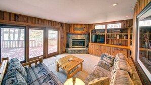 A cozy living room with a fireplace, wooden walls, a large window, and a bookshelf. - Pet Friendly Lakefront Cabin
 (Tafton)
