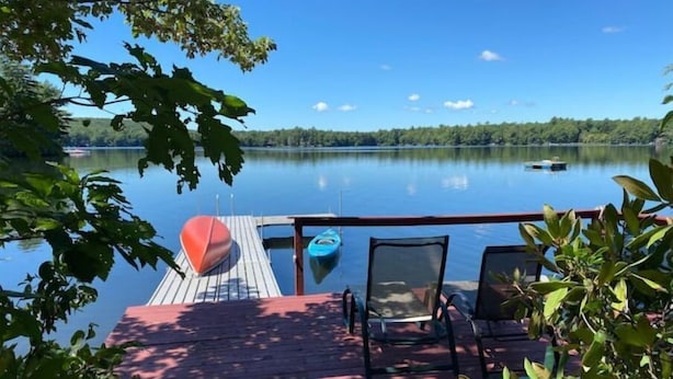 A wooden deck with a view of a calm lake, a red boat, and a kayak. - Pet Friendly Lakefront Cabin
 (Tafton)