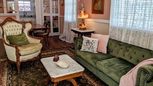A traditional living room with a green sofa, a tufted armchair, a marble coffee table, and a dining area with a white cabinet and chandelier. - Turn-of-the-Century Gem! The Painted Lady.   (Bisbee)