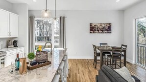 A modern kitchen with a marble countertop, wooden dining table, and a large window with a view of buildings. - Rooftop Deck w/ Grill/Golf!10min to Ole Opry & DT! (Nashville)