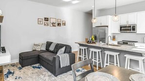 A modern living room with a grey sectional sofa, a kitchen with white cabinets and stainless steel appliances, and a bar area with stools. - Rooftop Deck w/ Grill/Golf!10min to Ole Opry & DT! (Nashville)