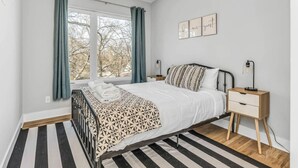 A bedroom with a bed, bedside tables, a window with curtains, and a view of trees outside. - Rooftop Deck w/ Grill/Golf!10min to Ole Opry & DT! (Nashville)