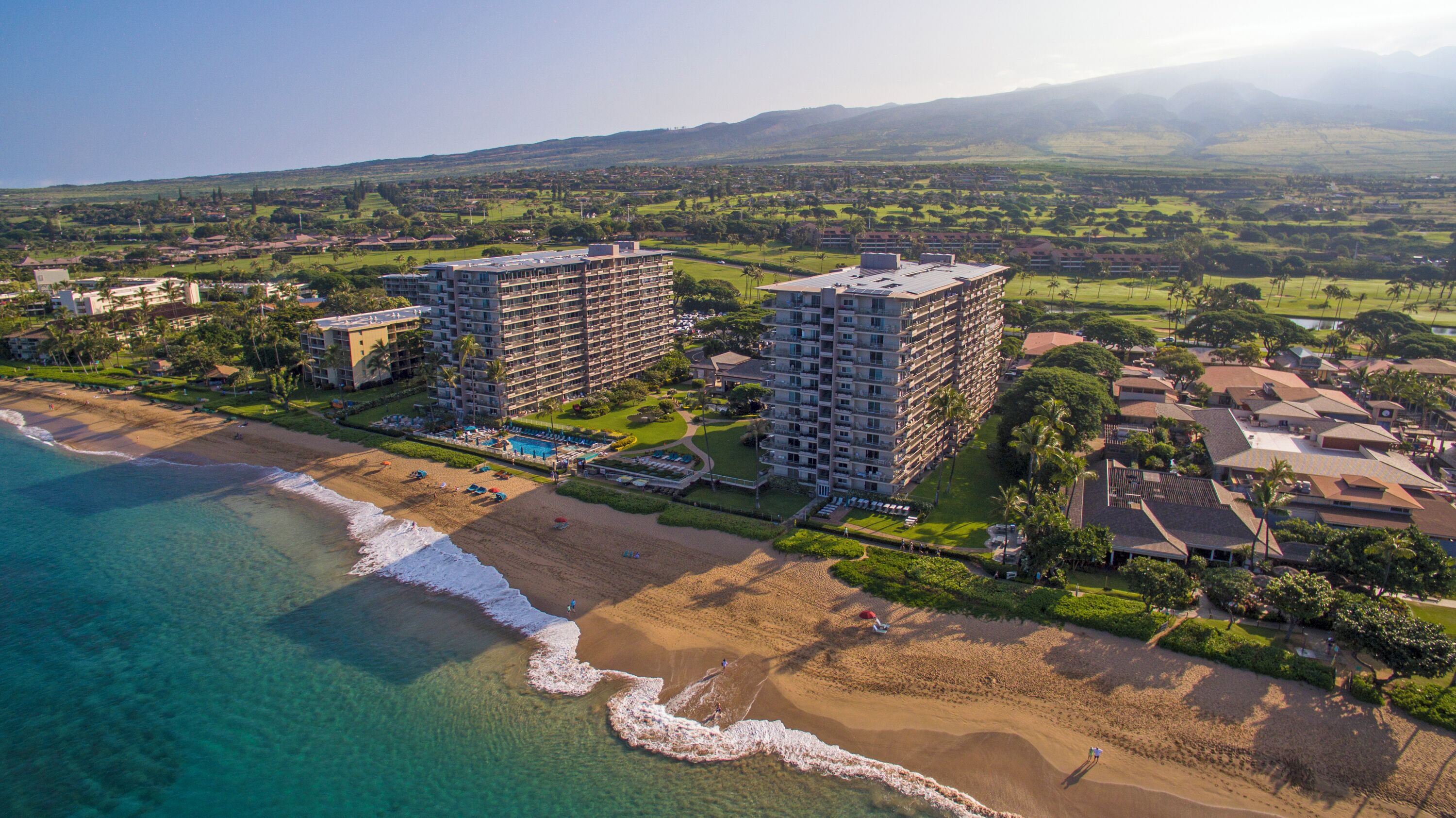 A coastal hotel with multiple high-rise buildings, a beach, and a golf course in the background.