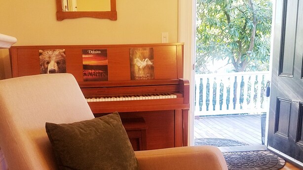 Un salon avec un piano, un fauteuil confortable et une vue sur un balcon doté d’une balustrade.