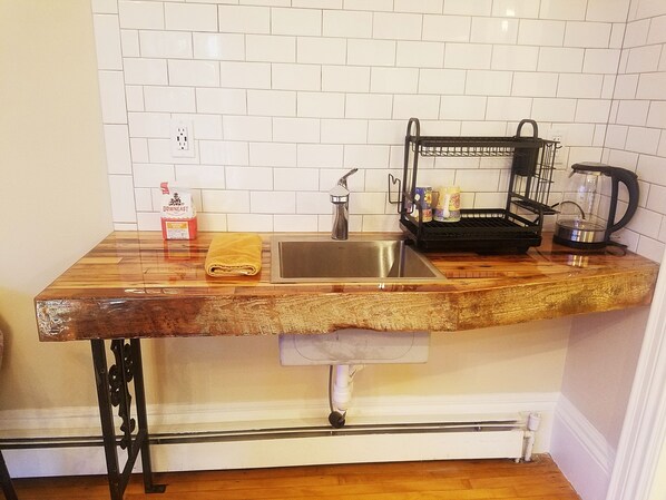 Una cucina con piano di lavoro in legno, lavello in acciaio inossidabile, macchina da caffè e bollitore.