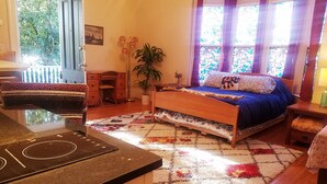 Une chambre à coucher avec un lit, un bureau, une chaise, une plante en pot et une fenêtre avec des rideaux.
