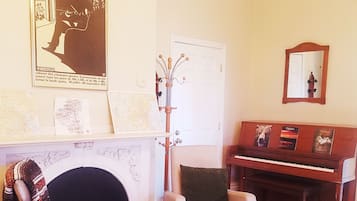 A living room with a fireplace, a piano, a chair, and a coat rack.
