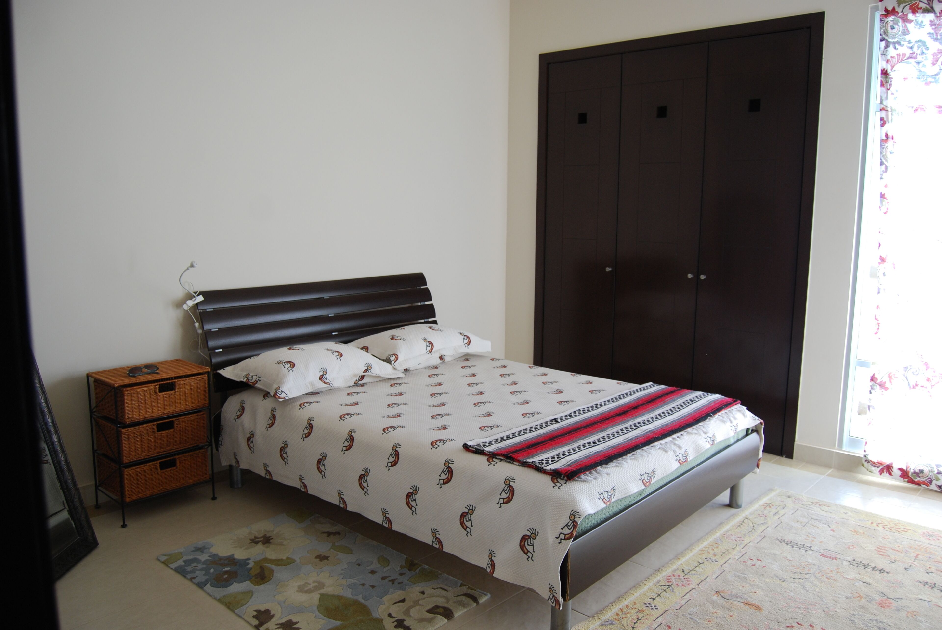 A bedroom with a bed, a wardrobe, a nightstand, and a window with curtains.
