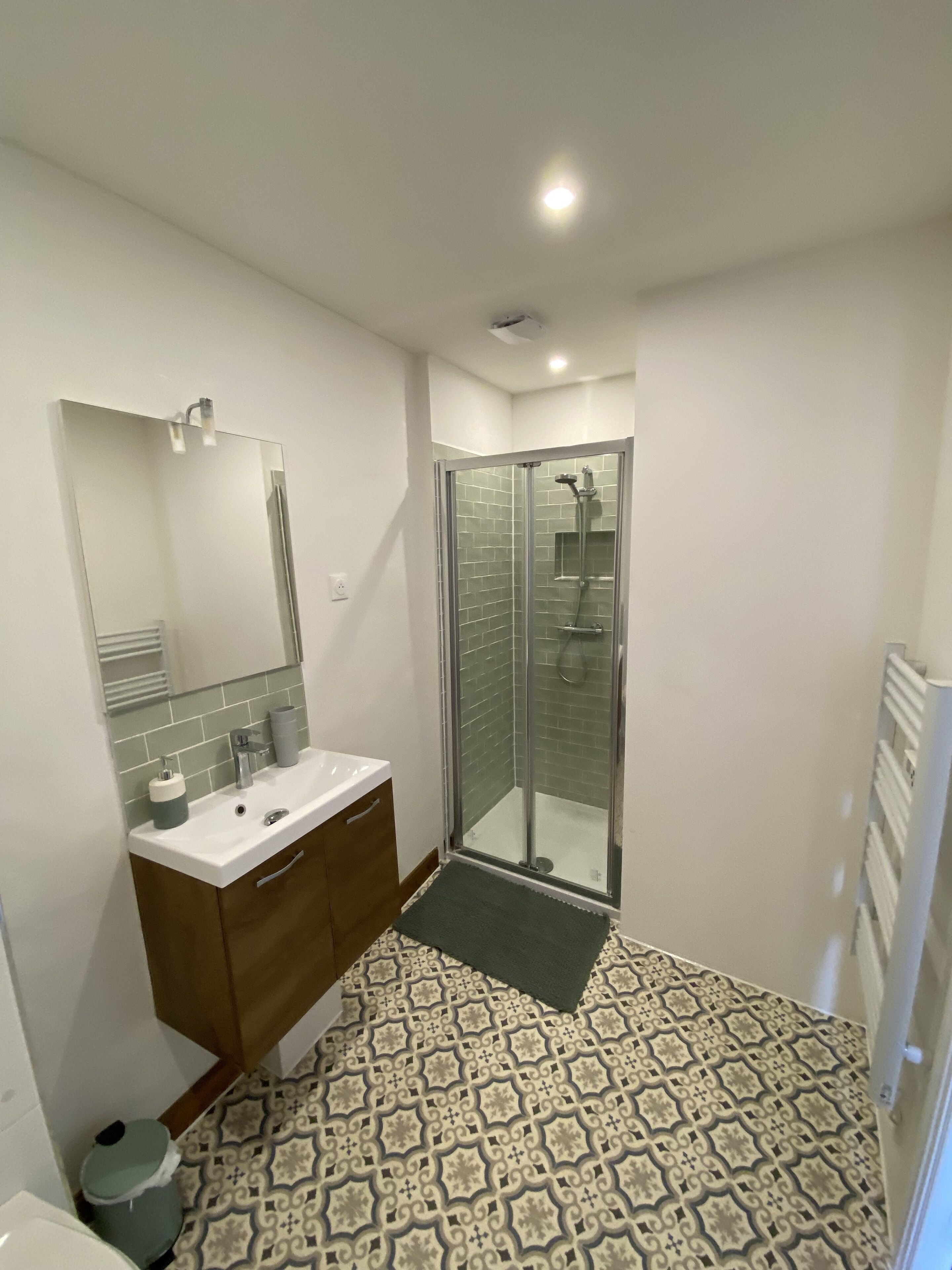 A modern bathroom with a glass shower enclosure, a white sink, and a patterned floor.