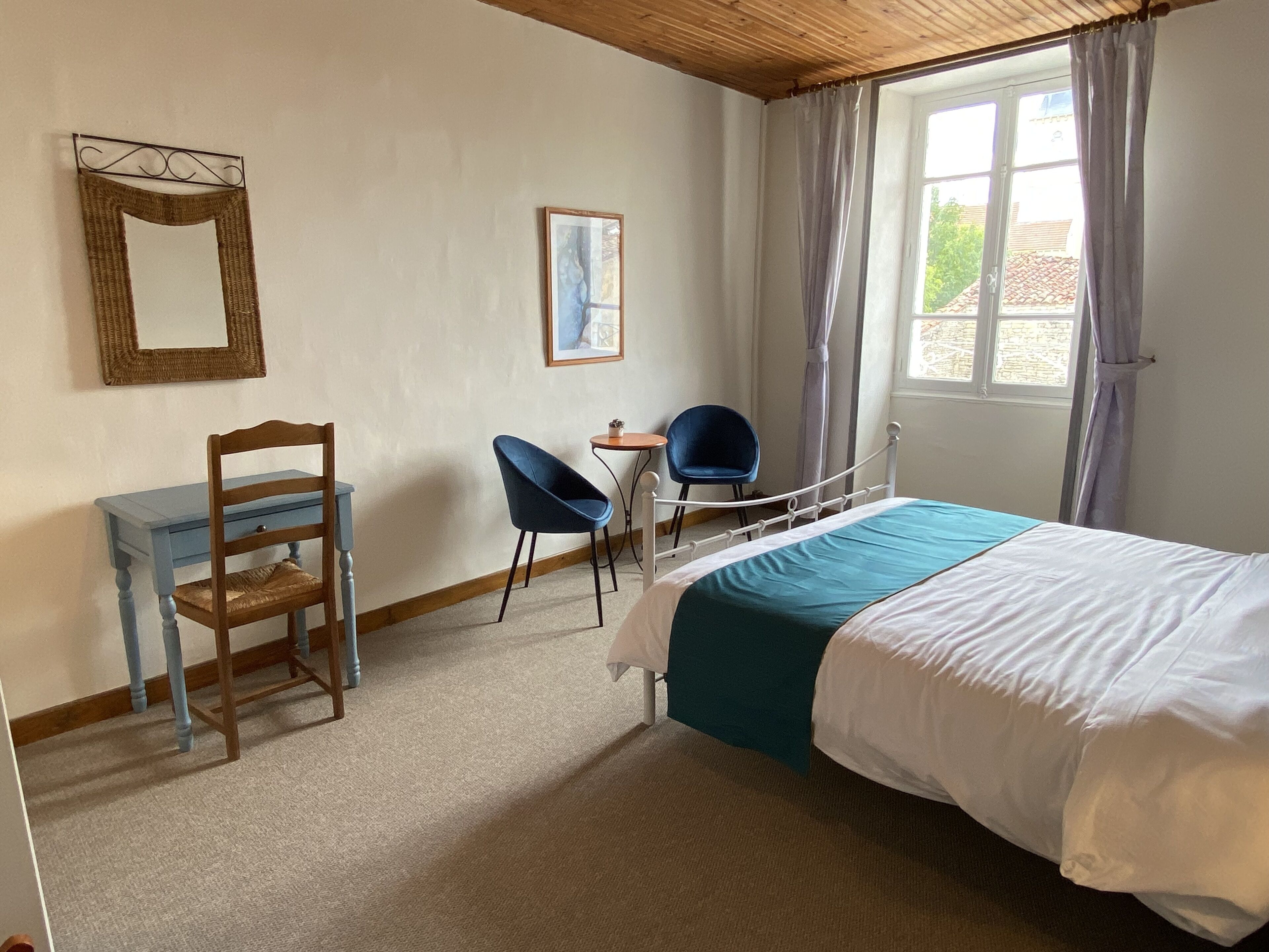 Een slaapkamer met een bed, een bureau, twee stoelen, een spiegel en een raam met gordijnen.