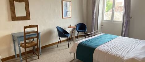 Une chambre à coucher comprenant un lit, un bureau, deux chaises, un miroir et une fenêtre avec des rideaux.