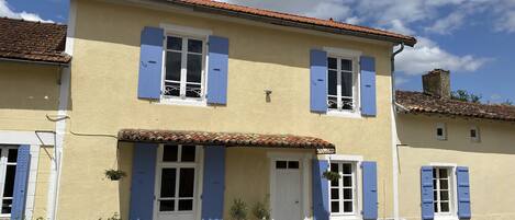 A two-story building with blue shutters, a tiled roof, and a gravel driveway.