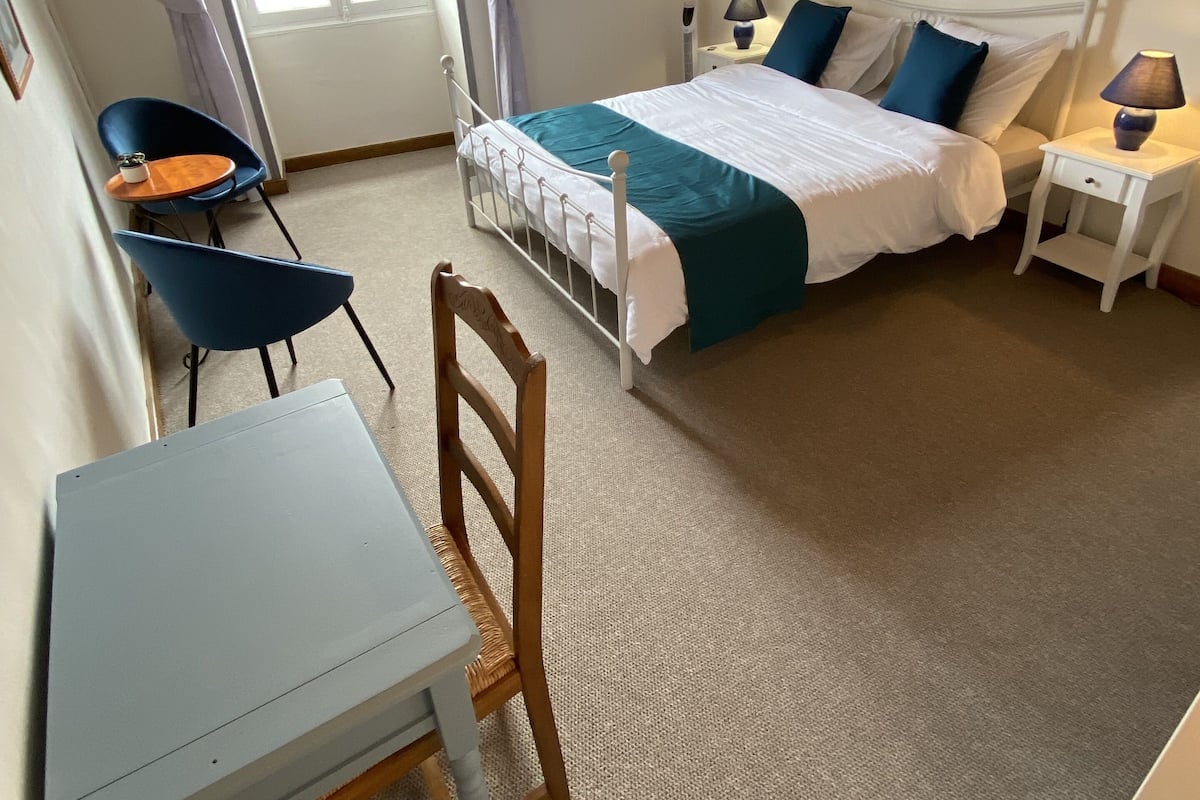 Een slaapkamer met een bed, nachtkastjes, een stoel, een bureau en een raam met gordijnen.