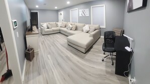 Una sala moderna con un sofá modular, una silla de oficina negra y un escritorio blanco con un ordenador.