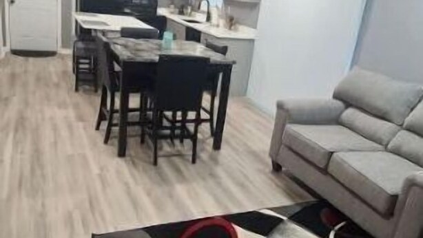 Una sala de estar moderna con un sofá gris, una zona de comedor con una mesa y sillas, y una cocina al fondo.