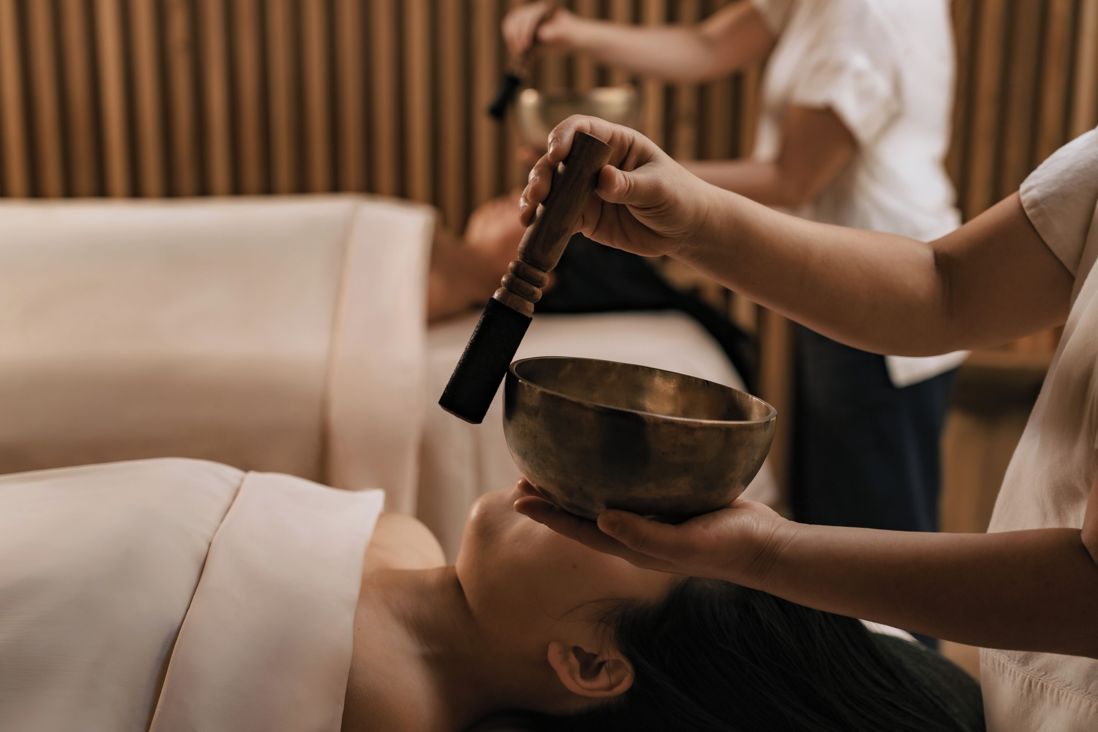 Eine Massageanwendung: Eine Person liegt auf einer Massageliege und erhält von einer anderen Person eine Kopfmassage.