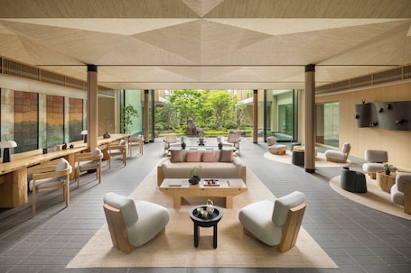 A spacious, modern lounge area with a central seating arrangement, large windows, and a view of a garden.