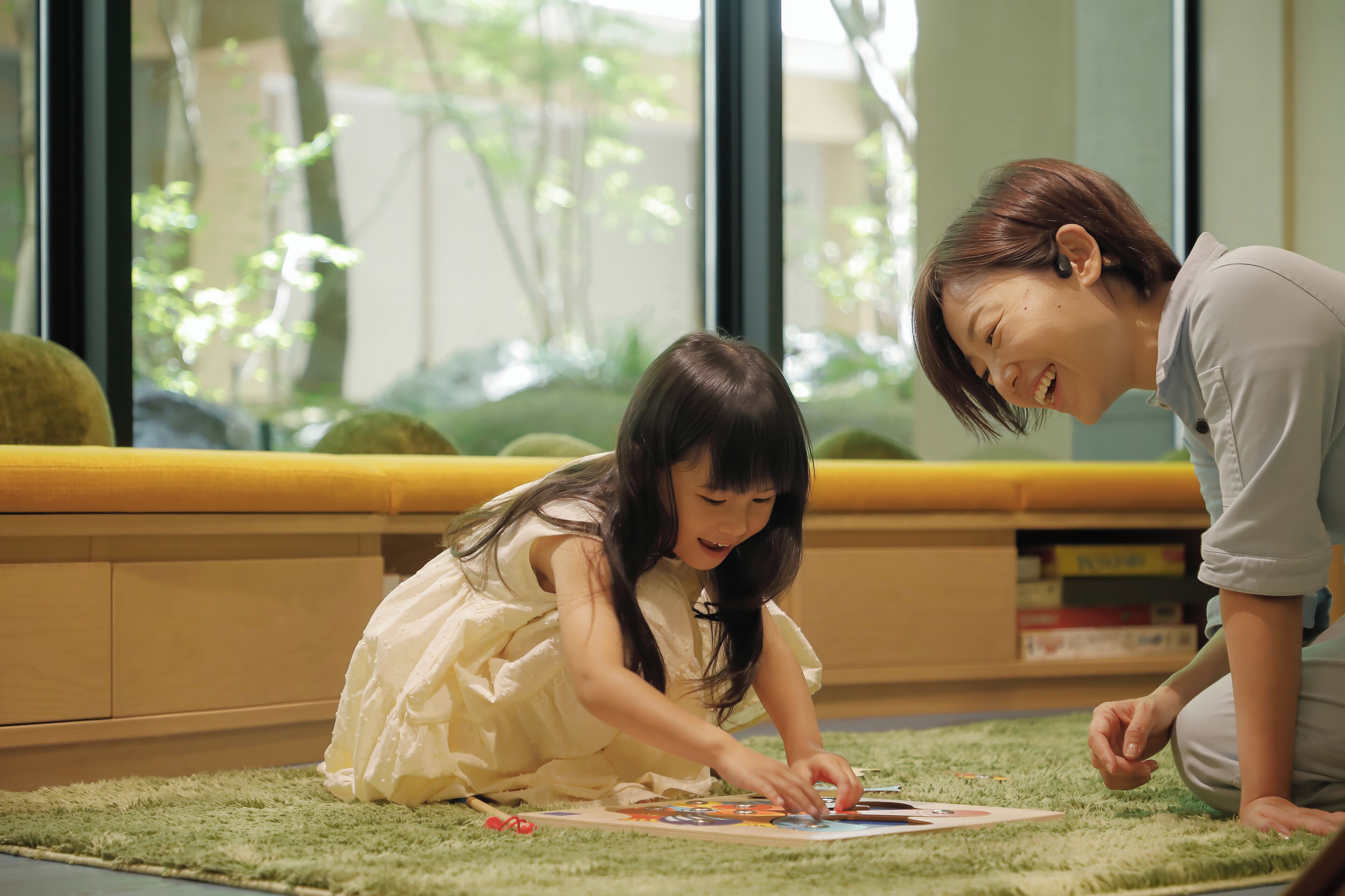 A child and an adult sitting on a carpeted floor, engaged in a puzzle activity.