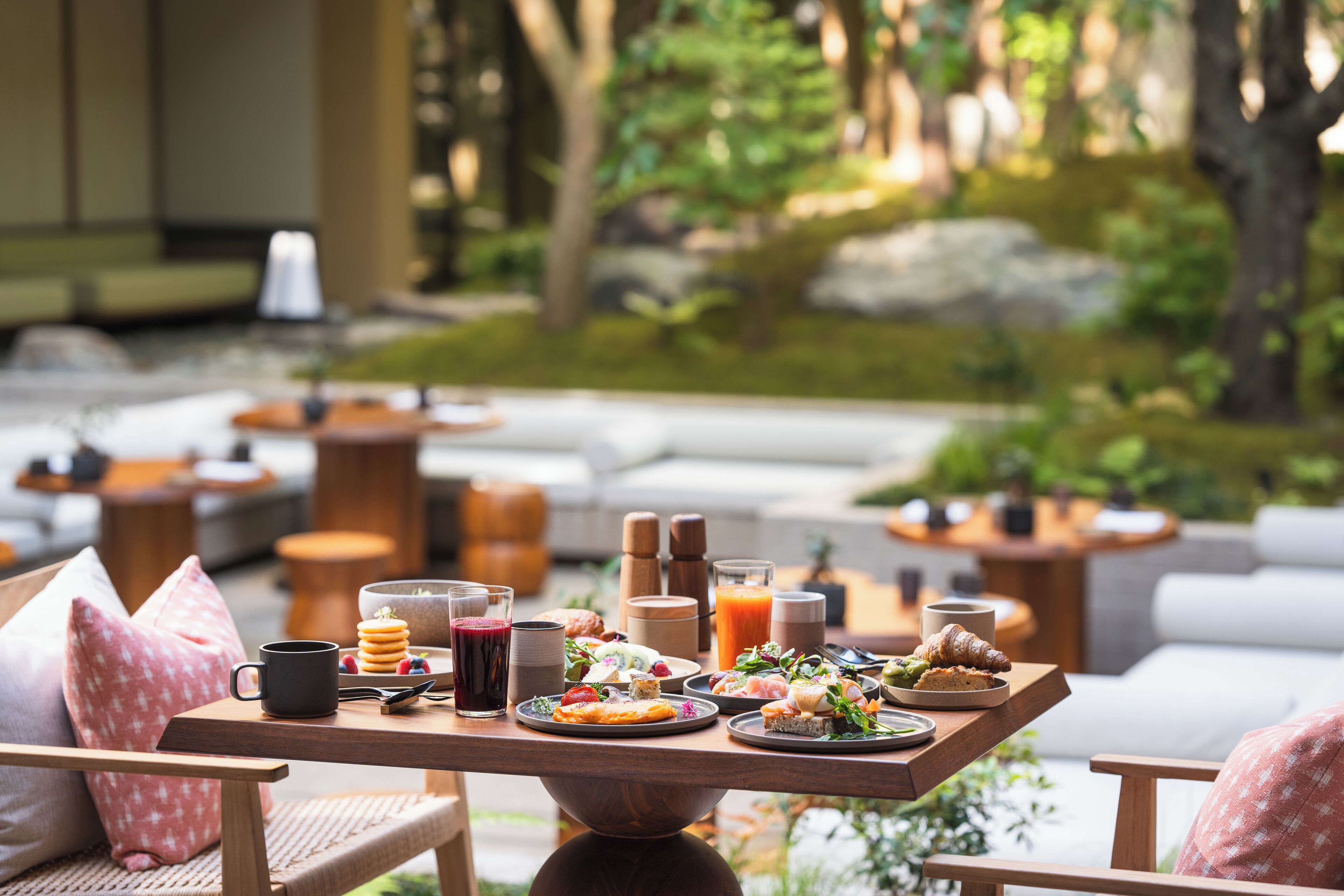 A breakfast table with various food items and drinks, set in a garden with outdoor seating.