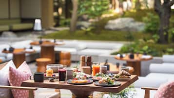 A breakfast table with various food items and drinks, set in a garden with outdoor seating.