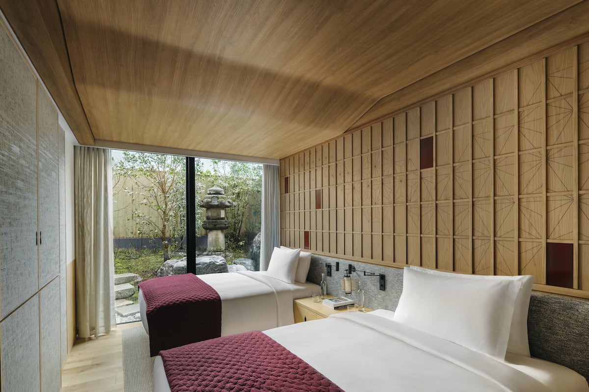 A modern hotel room with two beds, a wooden ceiling, a view of a garden, and a traditional Japanese-style wall panel.