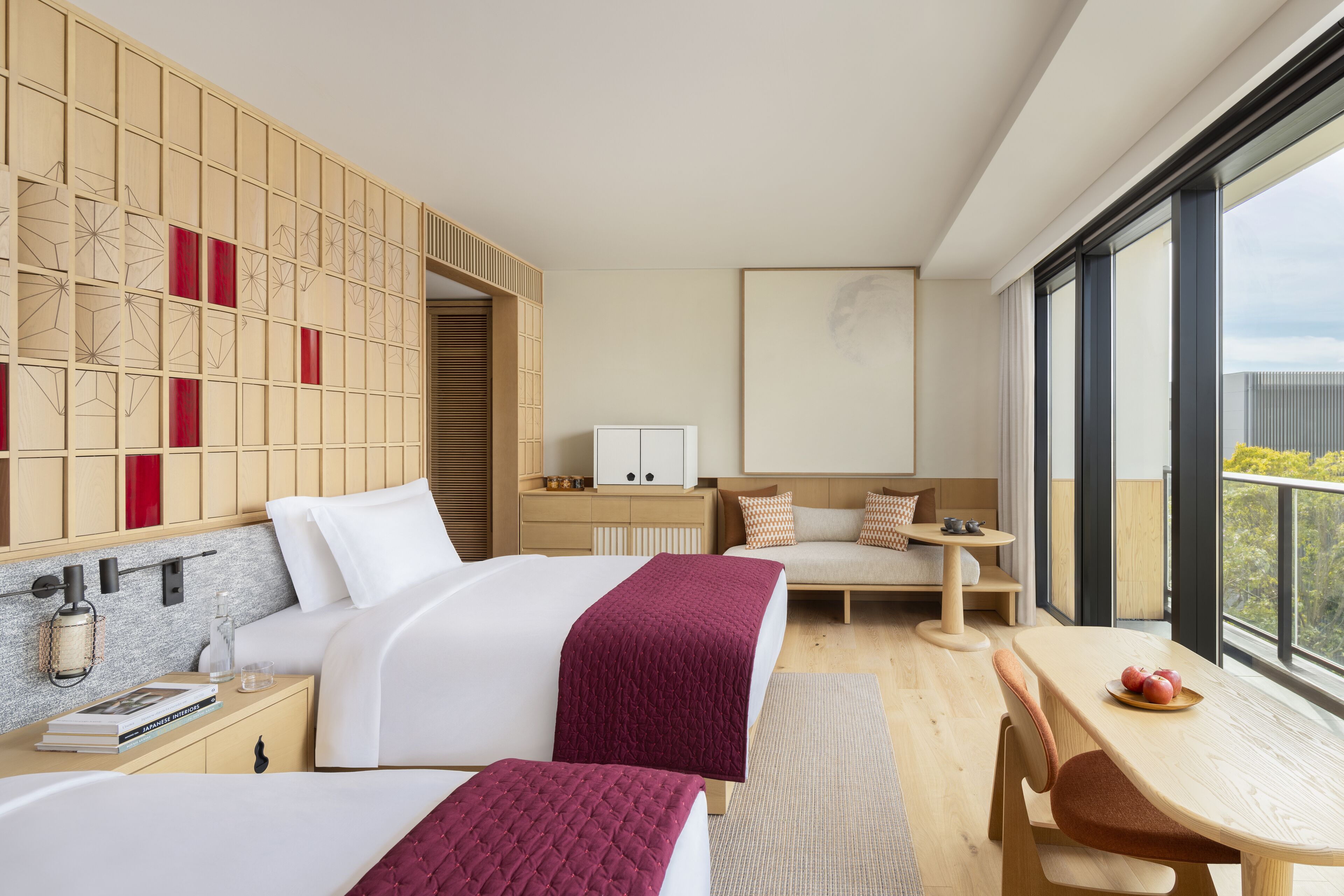 A modern hotel room with two beds, a dining table, a sofa, and a large window offering a view.