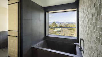 A modern bathroom with a large window, dark tiles, and a view of a cityscape.