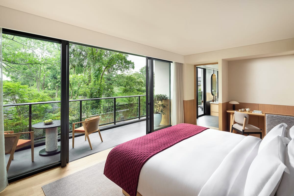 A hotel room with a large balcony, a bed, a desk, and a chair.
