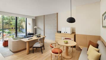 A modern living room with a wooden floor, a sofa, a dining table with chairs, and a kitchen area with cabinets and a refrigerator.