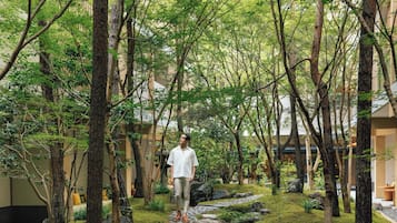 Un hombre caminando por un sendero de piedra rodeado de árboles en un jardín, con un edificio al fondo.